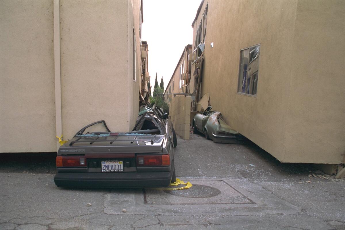 Closeup of a crushed car beneath the corner of a building.