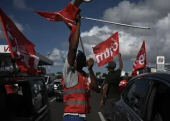 PHILIPPE LOPEZ/AFP Men in gilets wave flags of the French union CGT Martinique during aa go slow operation on the ring road leading to the airport in Fort-de-France, in the French Caribbean island of Martinique.