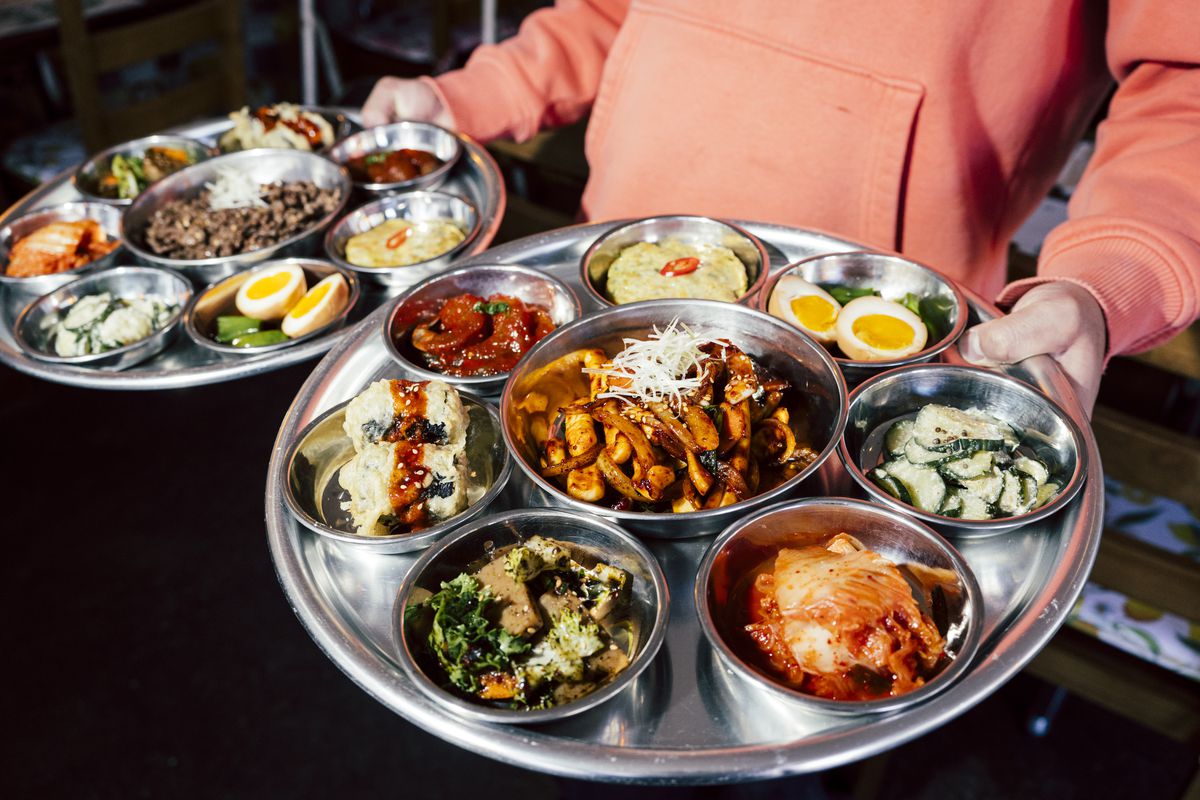 A person holds two large steel platters holding steel bowls of food.