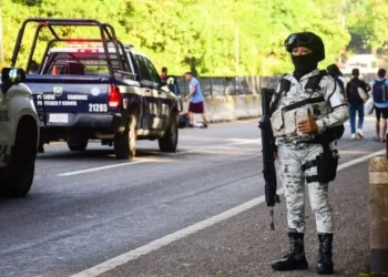 National Guardsperson in full uniform and carrying an automatic gun stands at duty on a street in Tapachula, Chiapas, filled with state police and national guard trucks