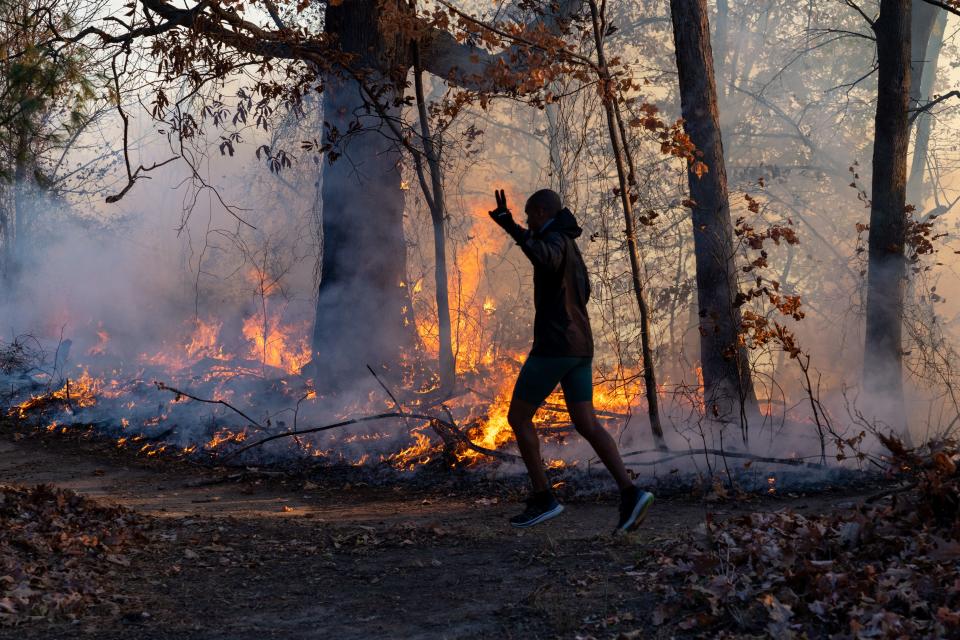 A morning jogger gestures as he runs past a fire lit by members of the New Jersey Forest Fire Service as it burns alongside Palisades Interstate Parkway in Englewood Cliffs, NJ. Back burning is a method used by firefighters to prevent a wild fire from extending.