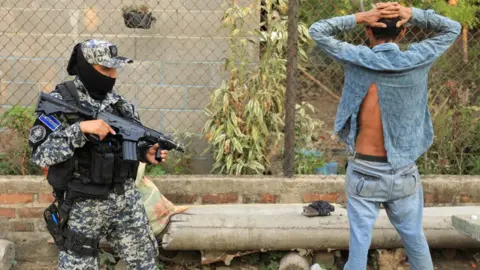 Reuters Police officer watches a man in a rural area of Nueva Concepcion after El Salvador's President Nayib Bukele announced the deployment of more than 5,000 security forces to the area after a policeman was killed in a gang attack, in Nueva Concepcion, El Salvador in this handout distributed to Reuters, May 17, 2023