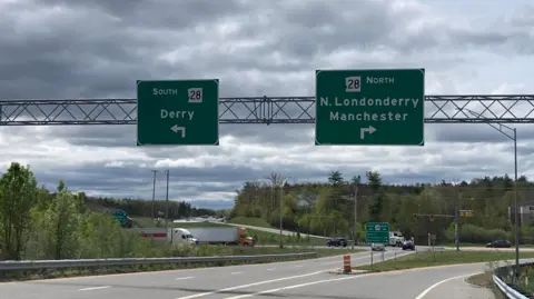 Sean Drysdale Two signs above a road in New Hampshire, one pointing left says south and Derry, the other pointing to the right says north N Londonderry and Manchester. There is a forest beside the road 