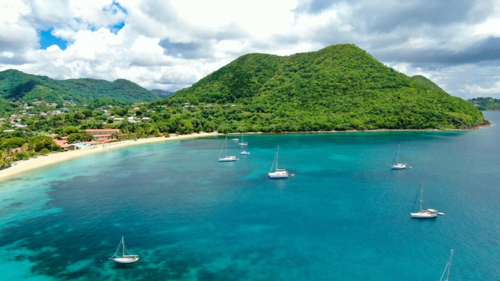 Aerial view of a few small boats on turquoise water near beach and green hills