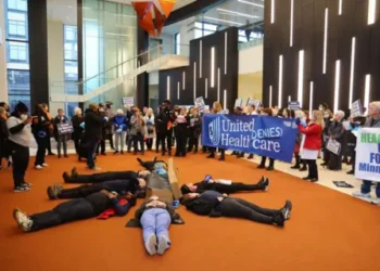 Getty Images Protesters with People's Action lay in circle at health insurance giant UnitedHealth Group's headquarters holding signs saying