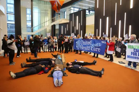 Getty Images Protesters with People's Action lay in circle at health insurance giant UnitedHealth Group's headquarters holding signs saying