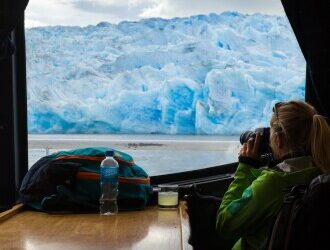 A woman looking out at glaciers through a camera from inside a cruise ship on  Patagonia’s waters.