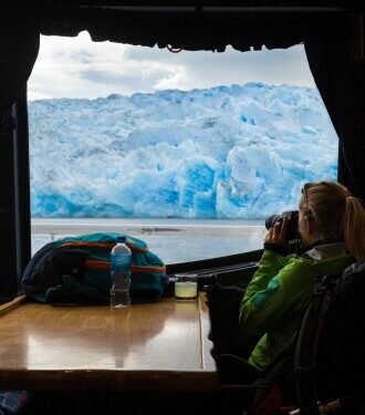 A woman looking out at glaciers through a camera from inside a cruise ship on  Patagonia’s waters.