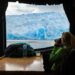 A woman looking out at glaciers through a camera from inside a cruise ship on  Patagonia’s waters.