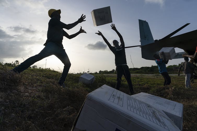 Aid workers in silhouette tossing boxes of food down a human chain.