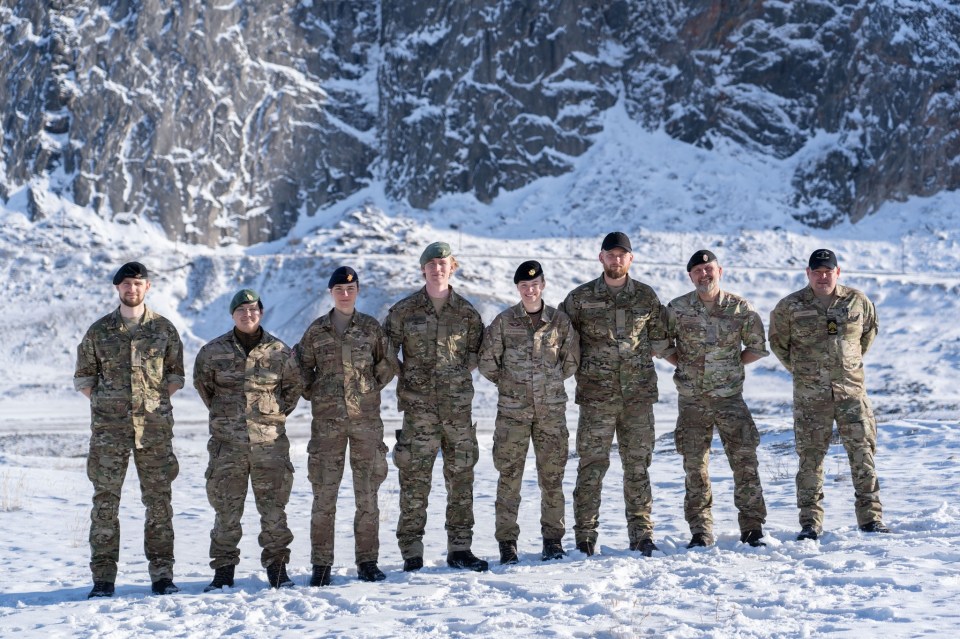 Eight Danish soldiers in camouflage uniforms stand in a snowy landscape.