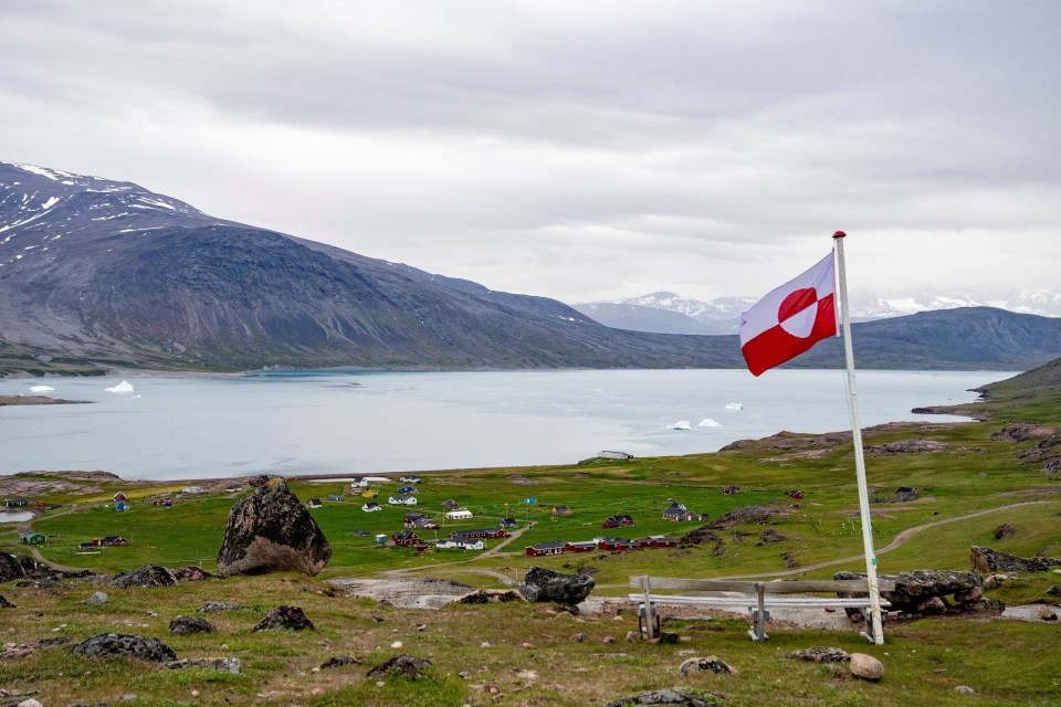 Greenlandic flag flying over a village by the water.