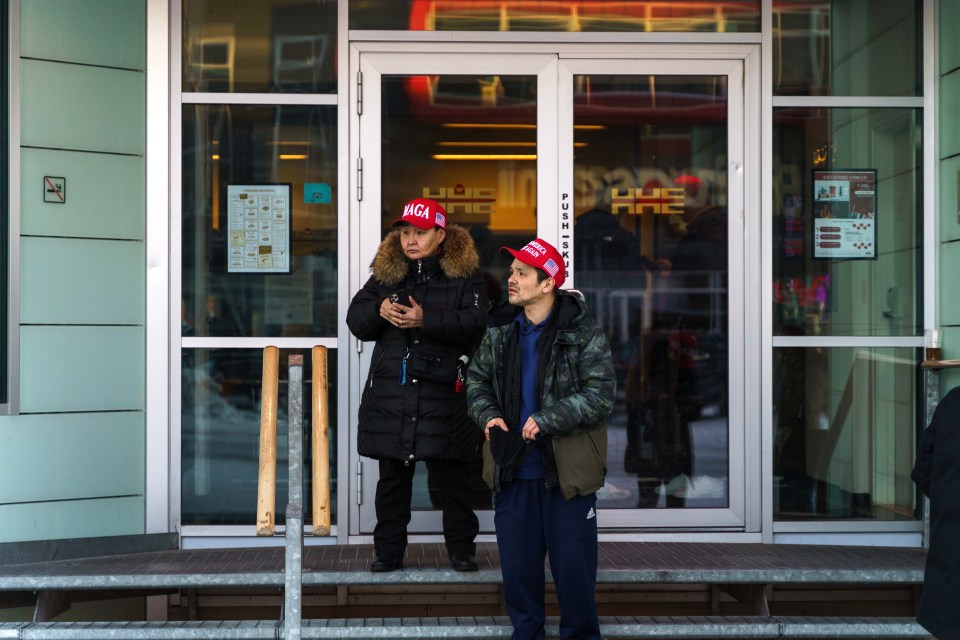 Two people wearing red MAGA hats stand outside a building.