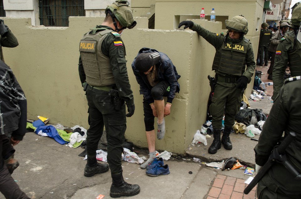 Police officers searching a person in a littered area.