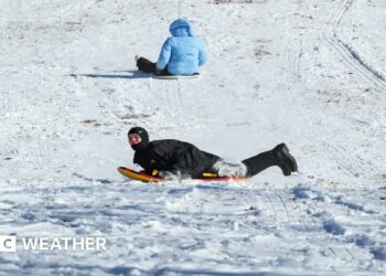 Two children slide down a snow covered hill on sledges