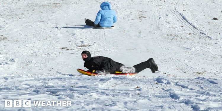 Two children slide down a snow covered hill on sledges