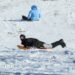 Two children slide down a snow covered hill on sledges