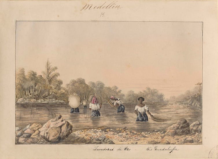 Five dark-skinned women dressed in white blouses and navy skirts are in a river holding large gold pans.