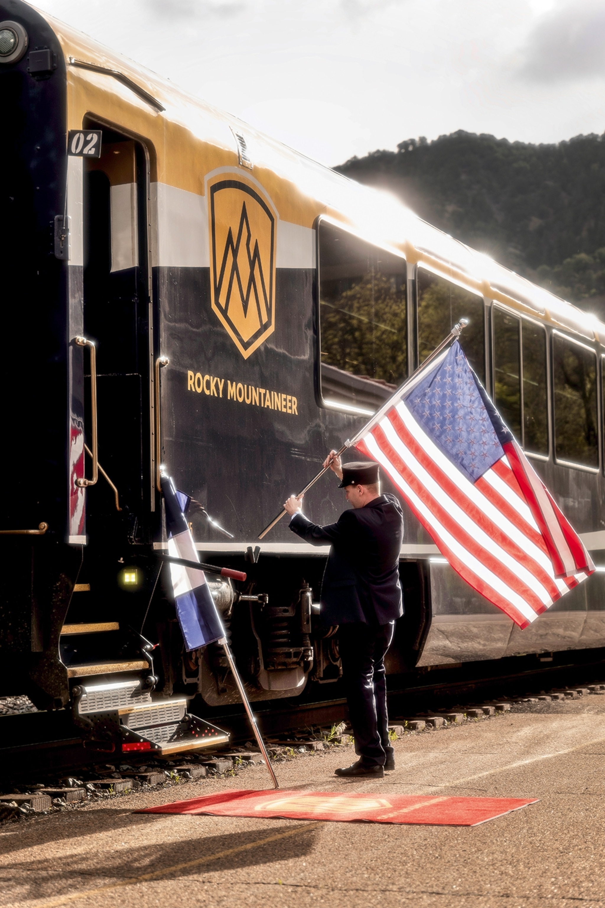 A train conductor waves an American flag on the side of a glossy train.