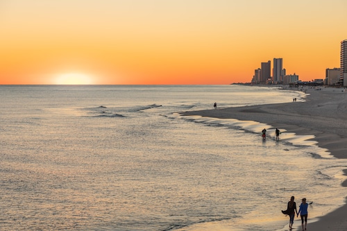 People walking and playing on the beach as the sun sets over the Gulf of Mexico at Gulf Shores, Alabama