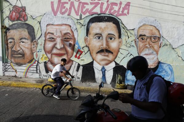 A cyclist rides past a mural depicting Dr. Jose Gregorio Hernandez, third from left, and other residents of La Pastora neighborhood in Caracas, Venezuela, after Pope Francis approved the canonization of the physician as Venezuela's first saint on Tuesday, Feb. 25, 2025. (AP Photo/Cristian Hernandez)