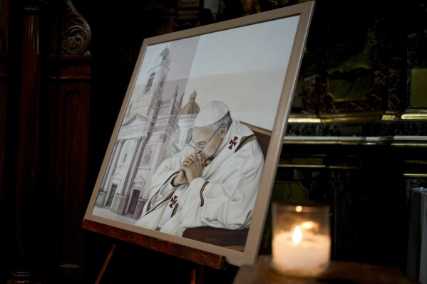 A candle glimmers alongside a painting of Pope Francis at San José de Flores basilica, Buenos Aires, Argentina, where he worshipped as a youth, Sunday, Feb. 23, 2025. (AP Photo/Natacha Pisarenko)