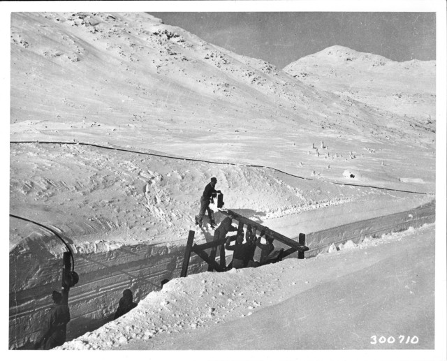 An Alaska Cable System crew lays submarine cable from flat cars along White Pass and Yukon Route Railroad.  During winter of 1946-47 the severe storms caused almost continued circuit outage so the cable is laid to replace the wire lines. 1...