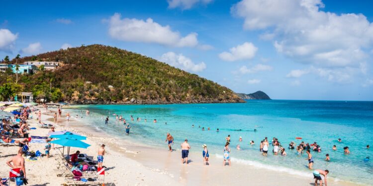 People on sand and in the turquoise waters of Coki Beach, with green hill in distance