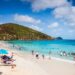 People on sand and in the turquoise waters of Coki Beach, with green hill in distance