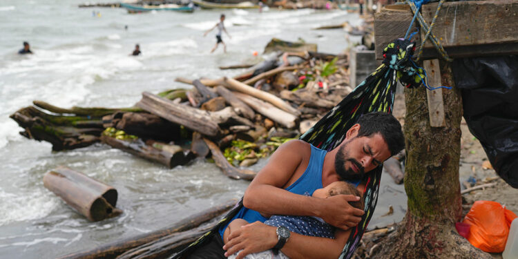 Venezuelan migrant holds his daughter while resting in a hammock