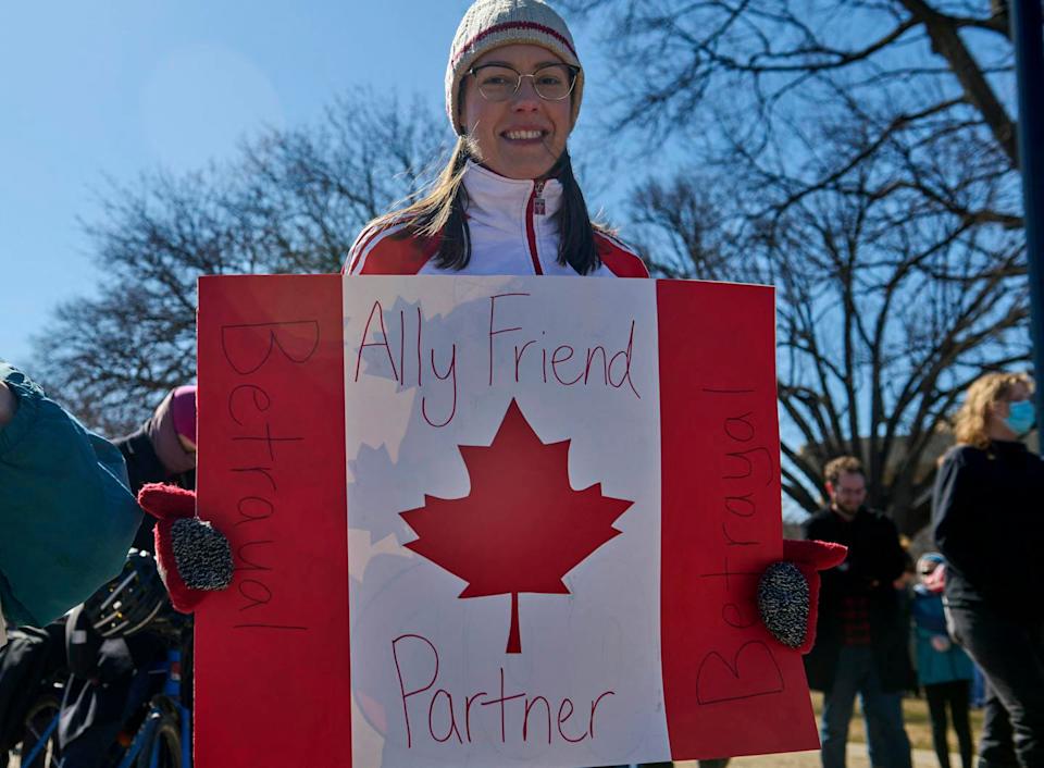 A person holds a sign decorated like the Canadian flag.